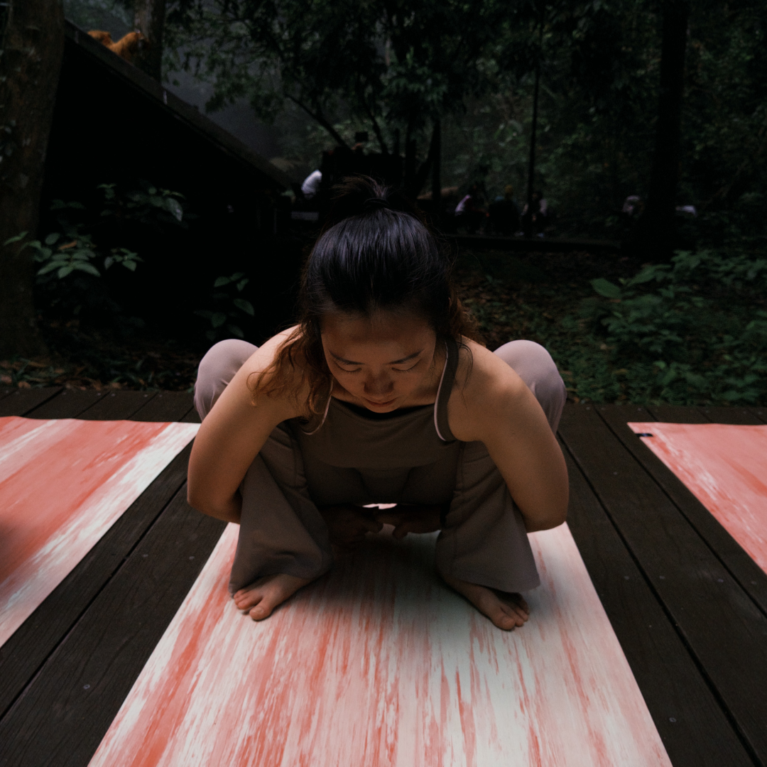 A woman in a Malasana yoga pose on a marbled Wolo Ascend yoga mat in an outdoor forest #color_unakite pink