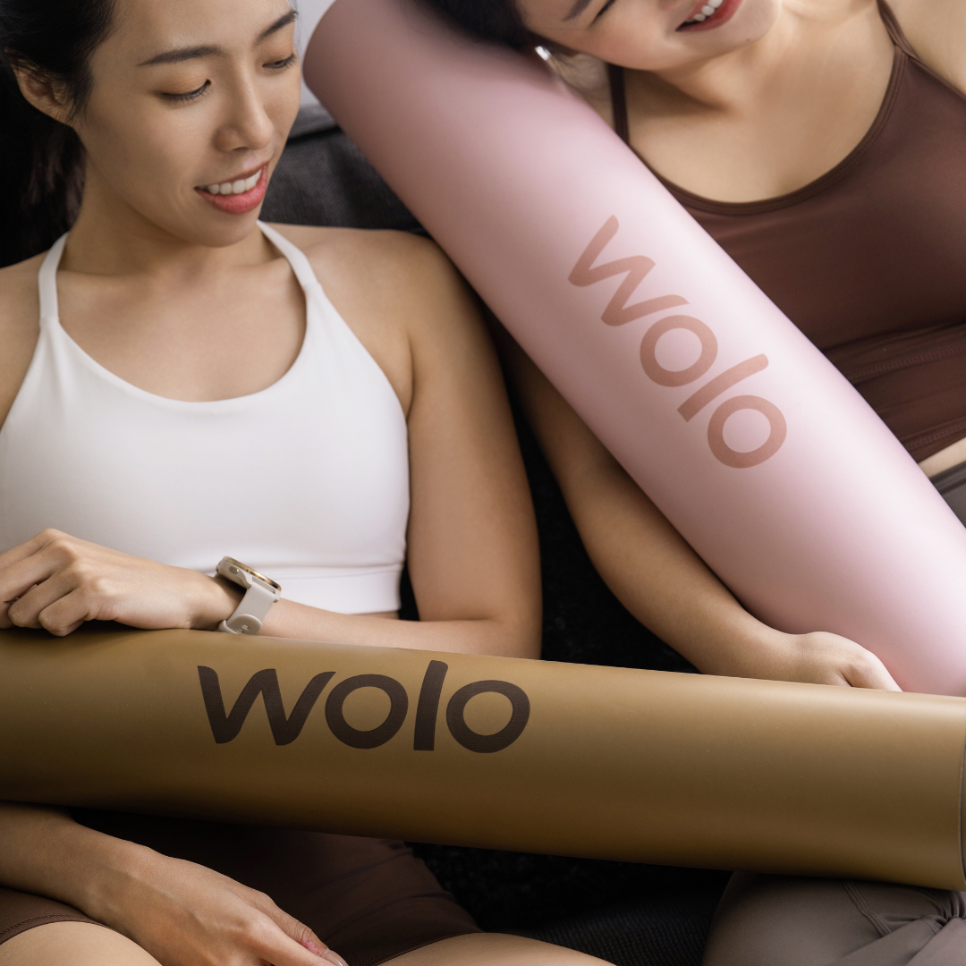 Two women holding two Wolo yoga mats, one khaki and one pink