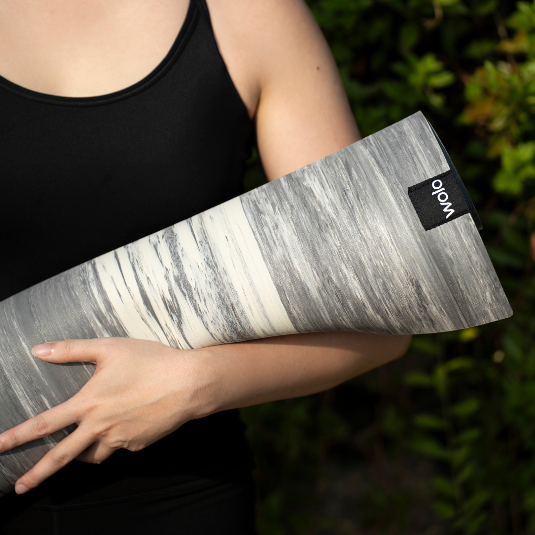 Person holding a gray marble-patterned yoga mat with a brand logo.