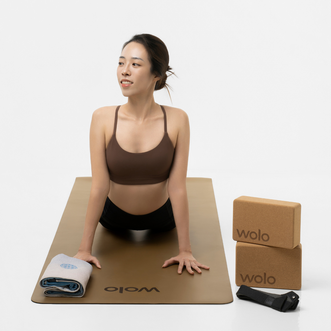 Woman practicing yoga with a Wolo brand mat and block on a white background