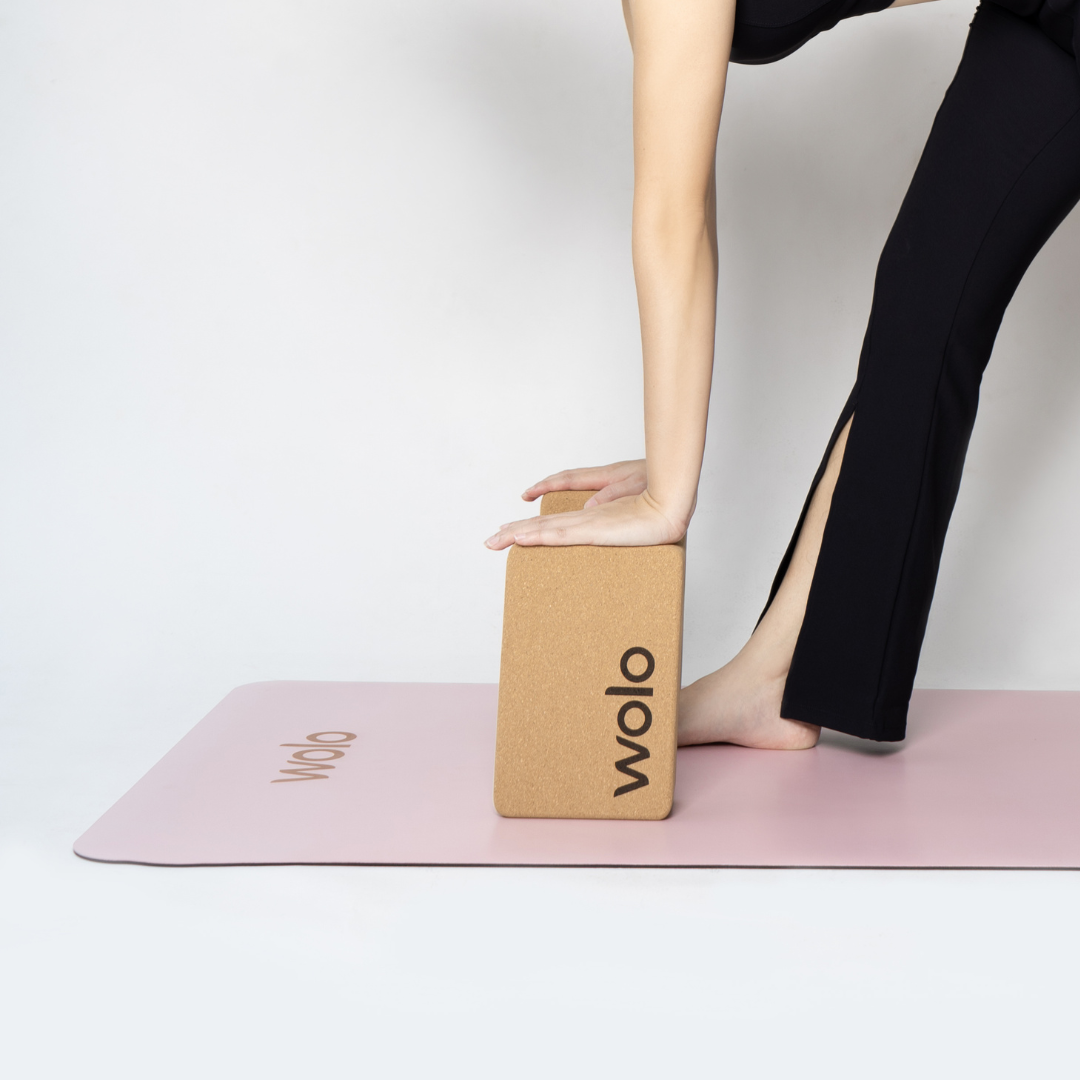 Person using a yoga block on a pink mat with 'wolo' branding.