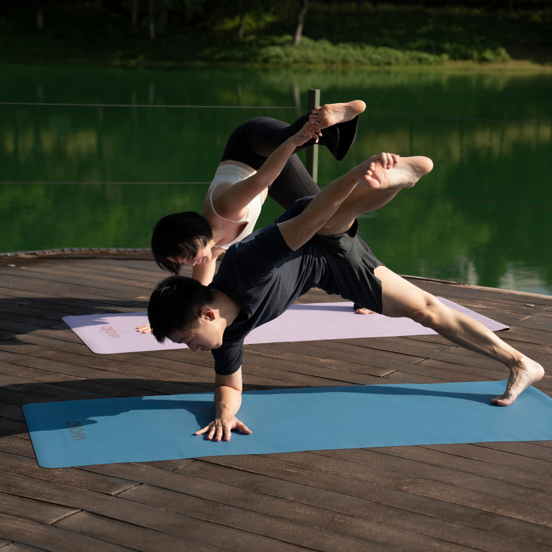 Two people practicing yoga on a wooden deck by a lake.