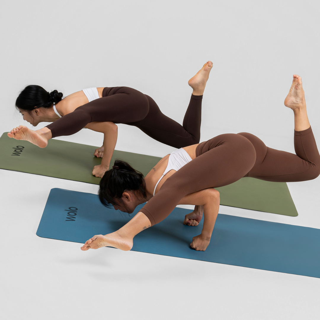 Two women practicing yoga arm balance flying pose on green yoga mat