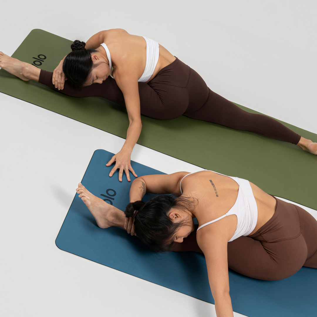 Two women stretching yoga pose front split forward fold on yoga mats