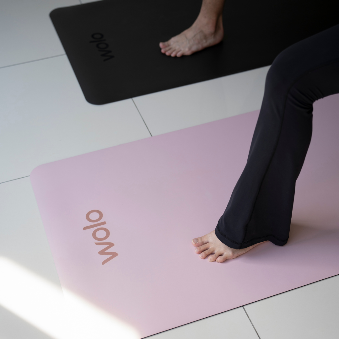 Person standing on a pink Wolo yoga mat with another mat visible in the background.