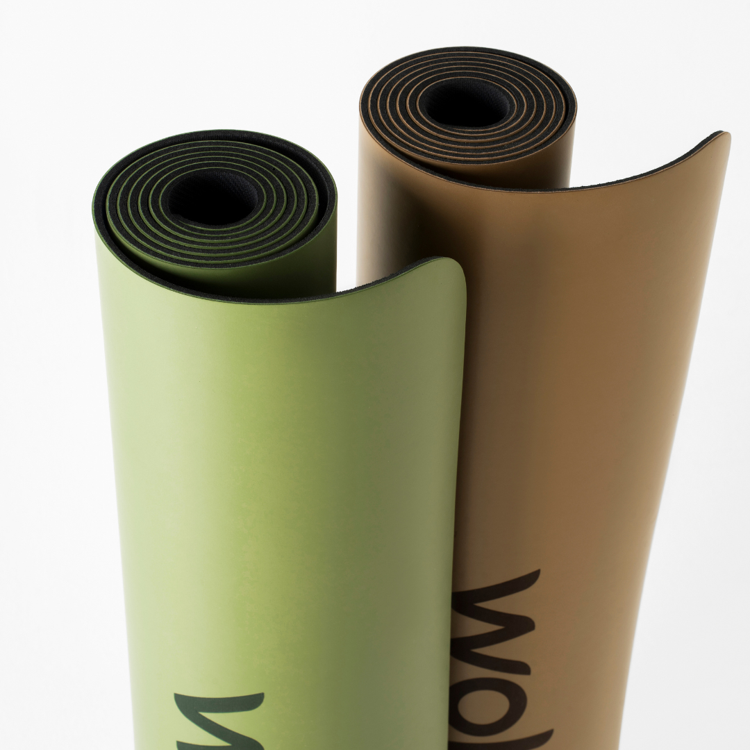 Two rolled-up high-quality natural rubber yoga mats, one green and one brown, on a white background.