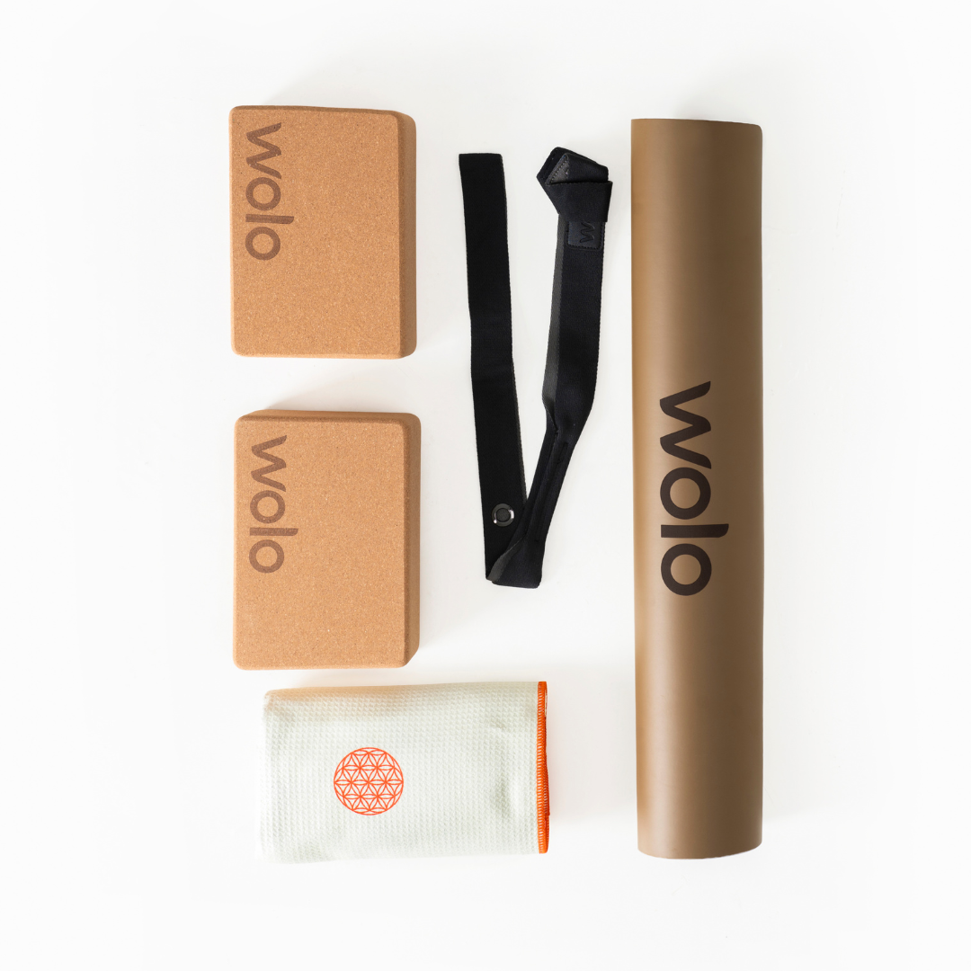 Wolo Yoga accessories including two brown yoga blocks, a black strap, a white mat with a red design, and a khaki mat on a white background.