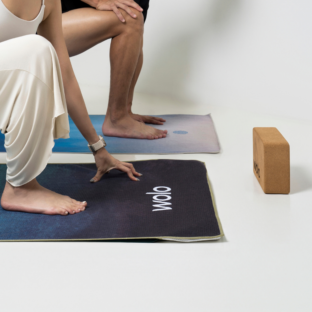 Two people on yoga mats with a yoga block on a white background
