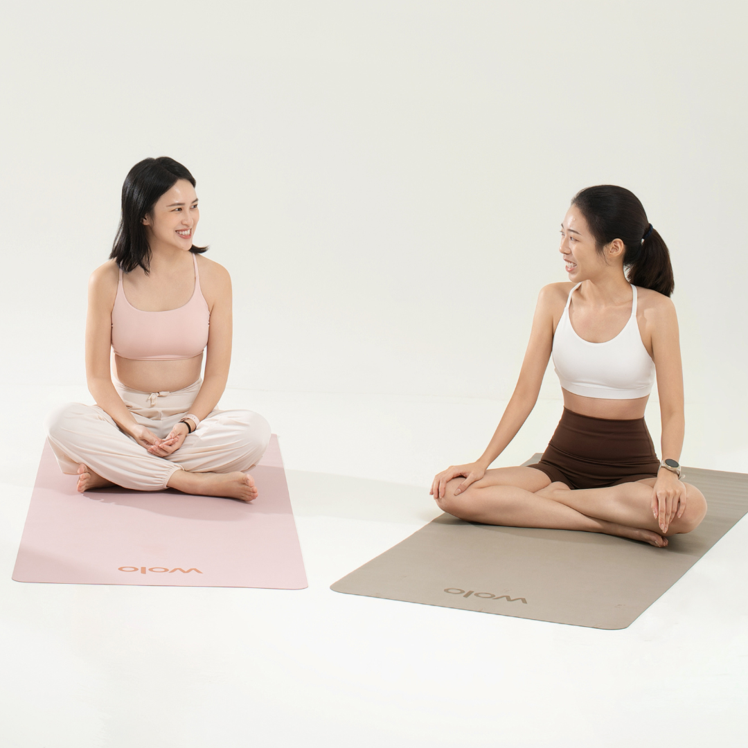 Two women sitting on yoga mats with a plain background